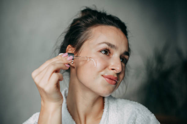 Brunette woman 30 years old applies serum on her face Brunette woman with long hair in a bun 30 years old applies serum on her face at home in the bathroom skin care stock pictures, royalty-free photos & images