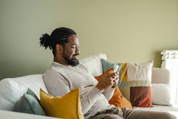 istock Young African-American man using mobile phone at home 1369335355