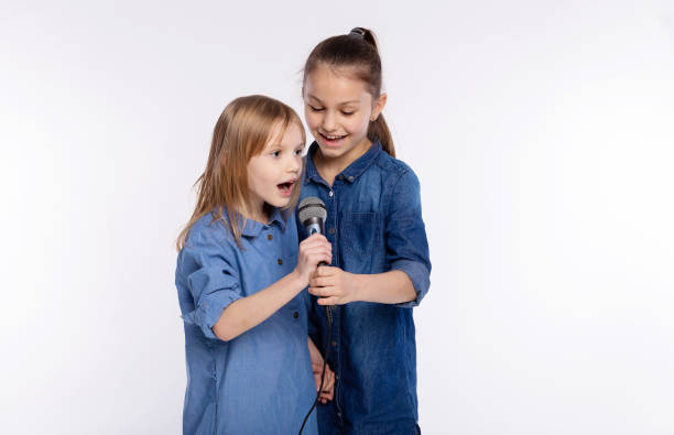 dos niñas de 6 y 8 años cantan una canción en un micrófono. el concepto es infancia, estilo de vida, música, canto, amistad sobre fondo blanco - 8 9 years studio shot friendship sibling fotografías e imágenes de stock