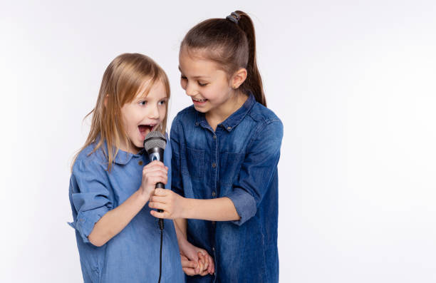 dos niñas de 6 y 8 años cantan una canción en un micrófono. el concepto es infancia, estilo de vida, música, canto, amistad sobre fondo blanco - 8 9 years studio shot friendship sibling fotografías e imágenes de stock