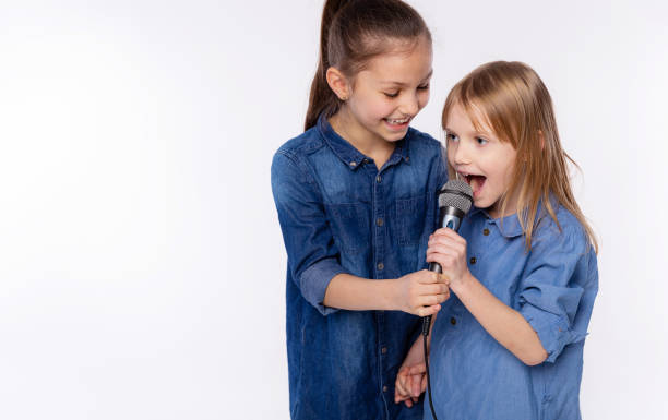 dos niñas de 6 y 8 años cantan una canción en un micrófono. el concepto es infancia, estilo de vida, música, canto, amistad sobre fondo blanco - 8 9 years studio shot friendship sibling fotografías e imágenes de stock