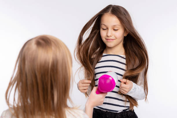 deux belles filles de 6 à 8 ans jouent avec le sèche-cheveux. les filles s’amusent à passer du temps ensemble et à sécher les cheveux sur fond blanc - female 8 9 years child excitement photos et images de collection