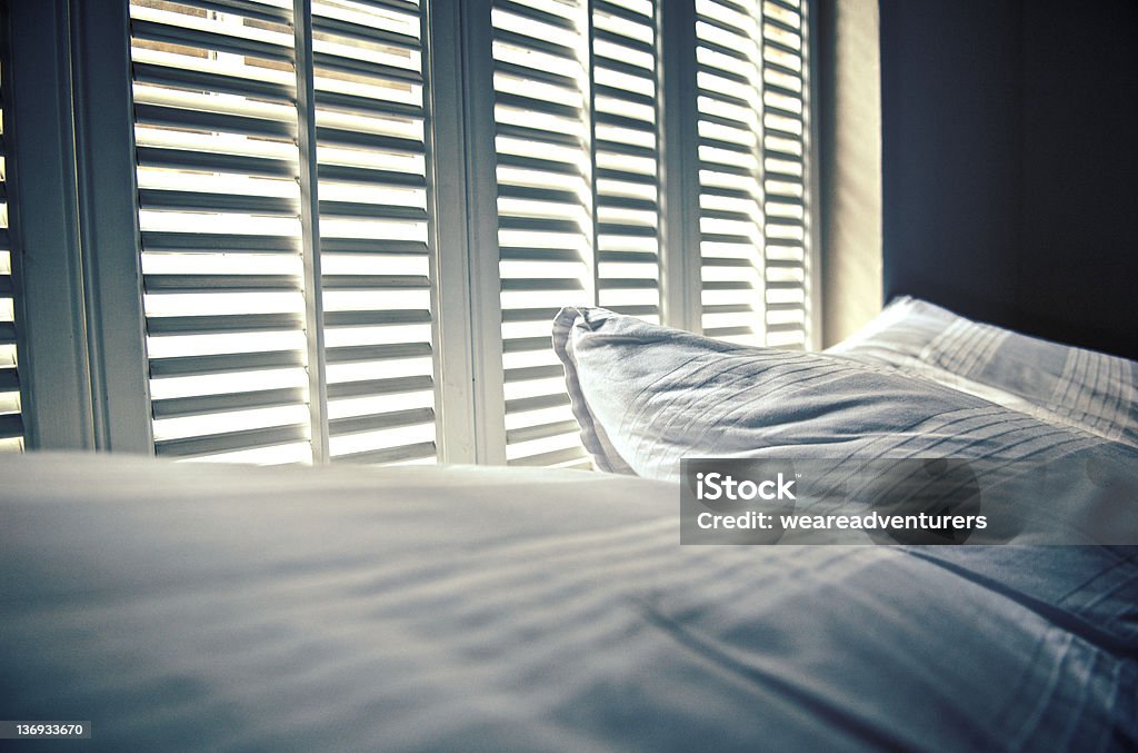 White linen against white shutters with white light behind Morning rays spill over the pillows. Shutter Stock Photo