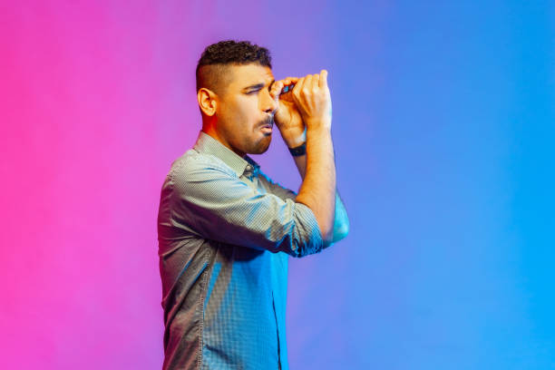 istock Man in shirt looking far away through monocular gesture, spying shocking content. 1369338987