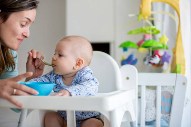 istock Cute little baby boy, eating mashed vegetables for lunch, mom feeding him 1369340147