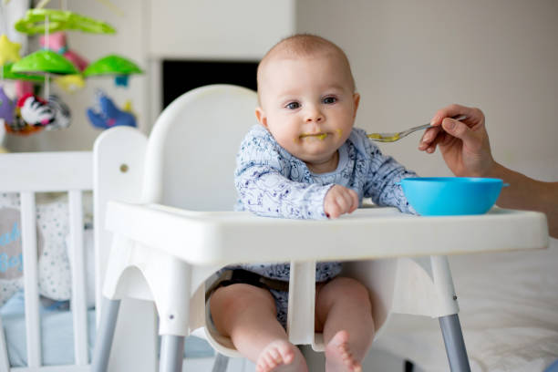 istock Cute little baby boy, eating mashed vegetables for lunch, mom feeding him 1369340174