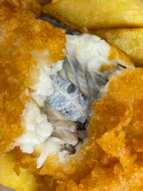 Full frame image of takeaway fish and chips with salt and vinegar seasoning, flakey white fish, unhealthy food takeout, greasy battered cod and deep fried chips, elevated view