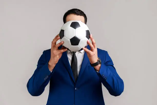 Photo of Portrait of unknown anonymous businessman supporting favorite team covering face with soccer ball.