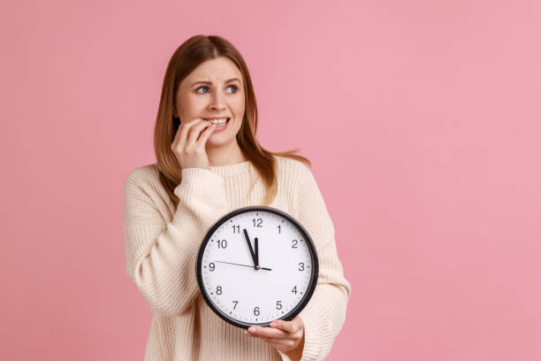 istock Woman holding big wall clock and biting her nails, need more time for work, deadline. 1369342165
