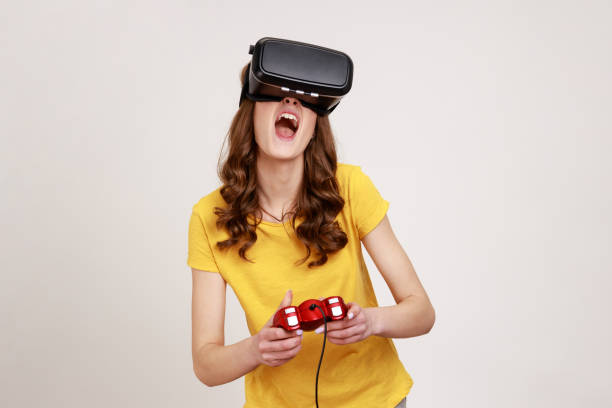 Excited screaming young woman in VR glasses playing video game, using simulator for education, yelling emotionally, wearing yellow T-shirt.