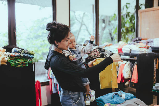 asian woman when carrying her baby showing shop owner clothing option asian woman when carrying her baby showing shop owner clothing option baby boutique stock pictures, royalty-free photos & images