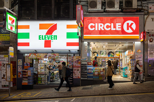 Hong Kong - February 8, 2022 : People walk past the Circle K and 7-Eleven convenience stores in Hong Kong. Both are international chain of convenience stores.