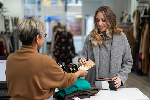 Young blonde woman paying in cash at the clothing store with a fifty euro bill to the clerk