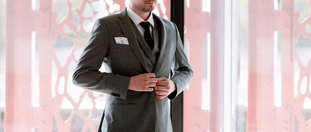 Handsome Man get dressed for the special event or important meeting. Young confident Guy wearing grey suit and tie, preparing formal elegant wear. Copy space
