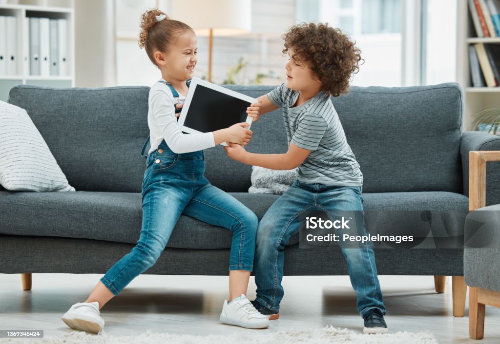 Shot of two siblings fighting in a game of tug of war over their digital tablet But it's my turn Fighting Stock Photo