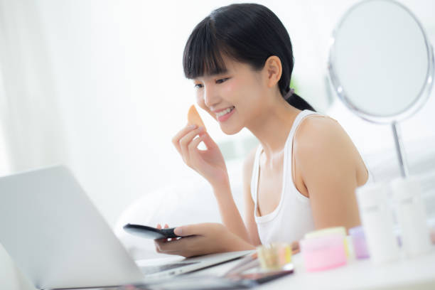 beauté de jeune femme asiatique avec maquillage d’apprentissage avec bouffée de poudre sur la joue regardant l’ordinateur portable avec tutoriel cours en ligne, enseignement féminin et expliquer le maquillage avec cosmétique sur les médias en stre - stage makeup women beauty human face photos et images de collection