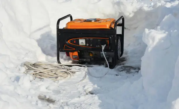 A mobile portable backup generator on the snow after a winter storm. Using a portable generator as an emergency power-supply during black outs in winter snow storms.