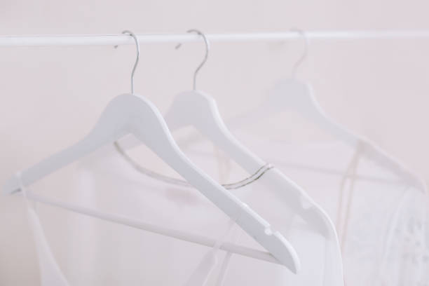white wooden hangers on a rod with white dress on a light wall background. Store concept, sale, design wooden white hangers on a rod with white dress on a light wall background. Store concept, sale, design clothes hanger rod stock pictures, royalty-free photos & images