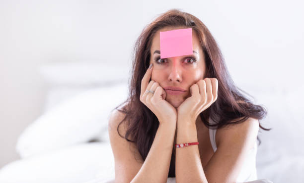 istock Woman who forgot something has pink postit on her forehead holding her head with both heads, thinking hard. 1369352195
