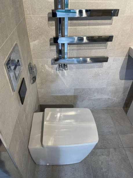 Stock photo showing close-up view of modern white luxury washroom suite with square toilet pan with integrated sensor lid and push button toilet flush plate and contemporary large, rectangular stone floor and wall tiles. imagen de la moderna suite de baño de lujo blanca, bandeja de inodoro cuadrada contemporánea con tapa de sensor integrada y placa de descarga del inodoro con botón pulsador, radiador de toallero calefactado cromado montado en la pared, gran pared rectan
