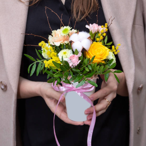 In women's hands is basket made of different flowers, roses, cotton, mimosa. An image for flower shop, postcard. Selective focus. stock photo