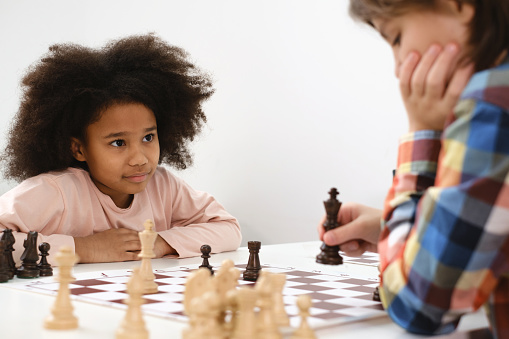 Diverse Group of kids playing chess. Concentrated multiethnic clever children with board game having fun at school. African American girl and Caucasian boys on chess lesson strategy