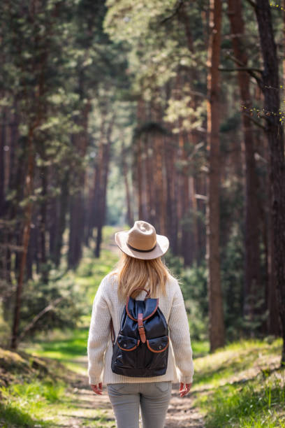 istock Woman with hat and backpack hiking on footpath in forest 1369356610
