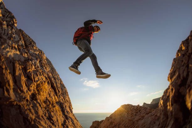 istock Sporty guy with backpack jumps from stone to stone 1369357334