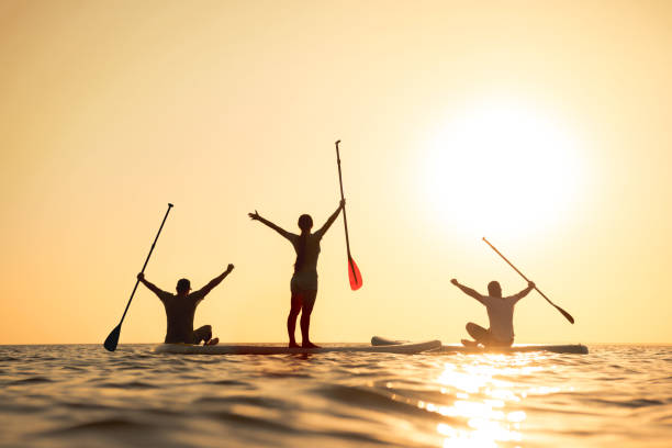 glückliche surfer auf sup-boards mit erhobenen armen - people in a row group of people in a row togetherness stock-fotos und bilder