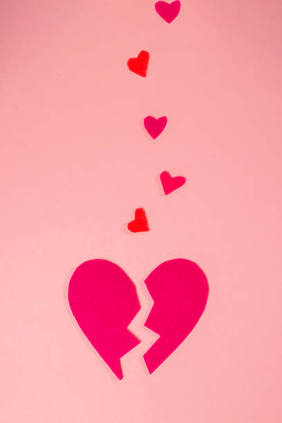 istock A broken heart. Felt heart divided into halves. Pink background, vertical orientation. Valentine's Day Concept 1369359829