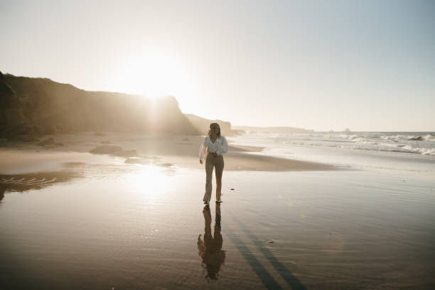 istock Young woman walking on a beach at sunset 1369359942