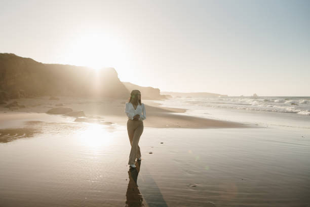 istock Young woman walking on a beach at sunset 1369359944