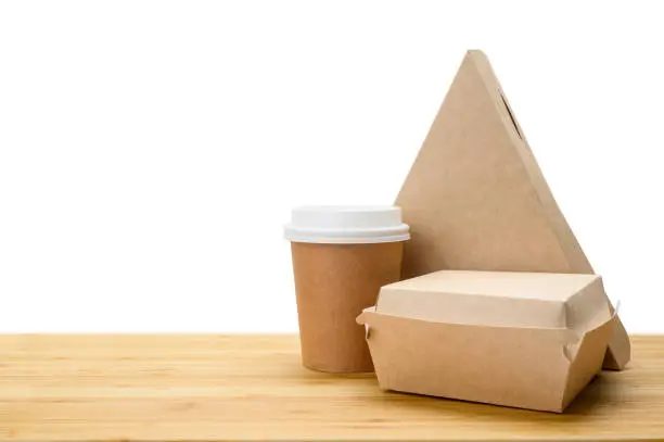 Photo of Lunch food delivery concept. Set of paper containers (pizza, hamburger, coffee paper cup) on a wooden table.