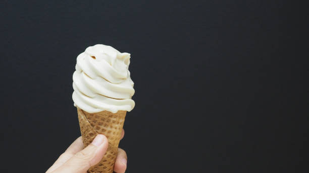 istock The hand is holding a soft-serve ice cream cone with a black background. 1369364365