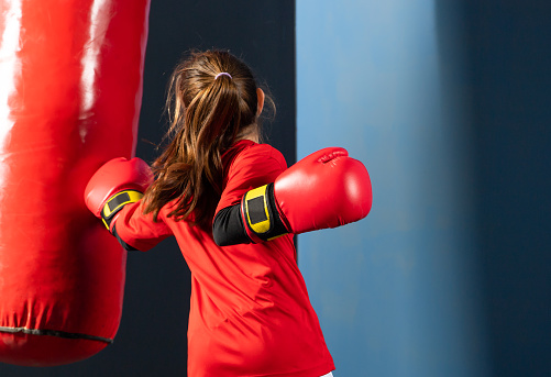 A girl in boxing gloves hits a punching bag in the gym.