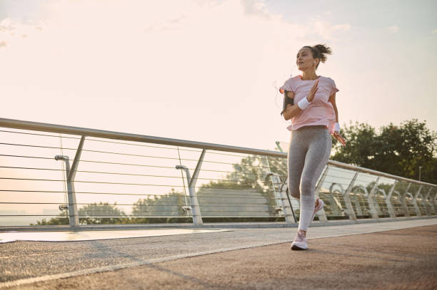 istock Young athletic woman, jogger, runner practicing sport outdoors, running fast along the bridge over the sunrise sky and river background. Healthy lifestyle concept. Workout jogging activity 1369365234