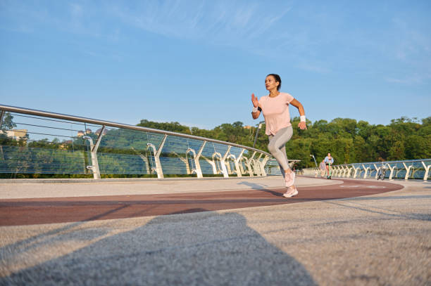 Determined athletic woman in sportswear runs on a treadmill over a city bridge. Sportswoman, female athlete runner doing morning jog at sunrise. Sport, cardio workout, healthy active lifestyle concept mujer atlética decidida en ropa deportiva corre en una cinta de correr sobre un puente de la ciudad. deportista, atleta corredora haciendo trote matutino al amanecer. deporte, entrenamiento cardiovascular, concepto de estilo de vida activo y saludable