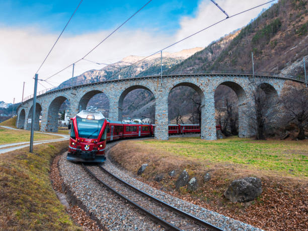 Bernina express train at the helical viaduct of Brusio. Brusio, Switzerland - February 3, 2022: Rhaetian Railway in the Albula and Bernina landscapes. Unesco heritage - Bernina express train at the helical viaduct of Brusio. helical stock pictures, royalty-free photos & images