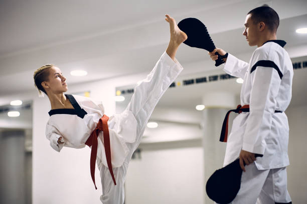 Determined martial artis with disability exercising high leg kick with her coach during taekwondo training. Taekwondo fighter with para-ability practicing high leg kick with her sparing partner at martial arts club. adaptive athlete stock pictures, royalty-free photos & images