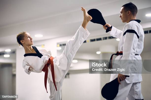 Determined Martial Artis With Disability Exercising High Leg Kick With Her Coach During Taekwondo Training Stock Photo - Download Image Now