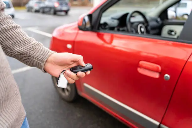 Male hand of young man holding electronic remote key pushing button near red rental car to open or close it. Travel, tour, tourism, journey, mode of transport, technology, ecology, car sharing.