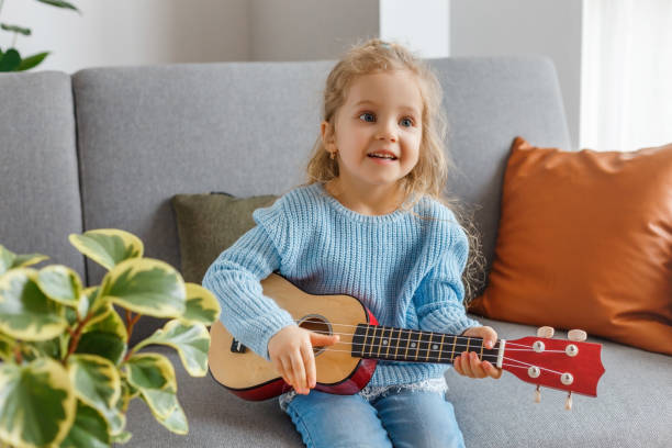 retrato de uma garotinha bonita tocando ukulele e cantando em casa. garoto de 3 anos aprendendo violão. conceito de educação infantil, hobby musical, talento, lazer pré-escolar feliz e paternidade. - preschool 2 3 years preschooler little girls - fotografias e filmes do acervo