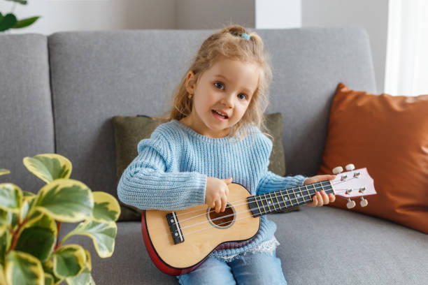 retrato de uma garotinha bonita tocando ukulele e cantando em casa. garoto de 3 anos aprendendo violão. conceito de educação infantil, hobby musical, talento, lazer pré-escolar feliz e paternidade. - preschool 2 3 years preschooler little girls - fotografias e filmes do acervo