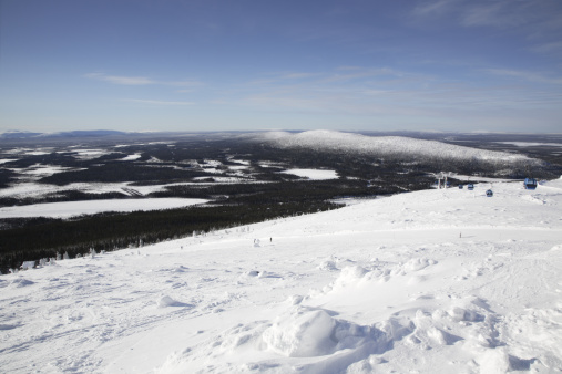 Top of Kätkätunturi fell, Levi, Finnish Lapland. Skiers and gondola making their way down the piste.