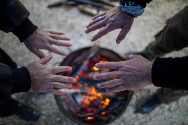 To warm it up, middle-aged man stretches his hands to the fire.