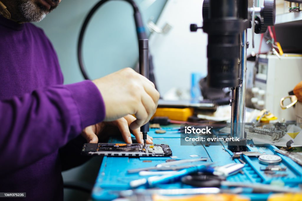 Technician disassembling smartphone with screwdriver. Repairing Stock Photo