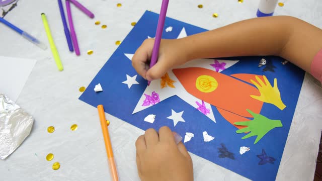 Child making rocket and stars from paper. Creative children play with craft.