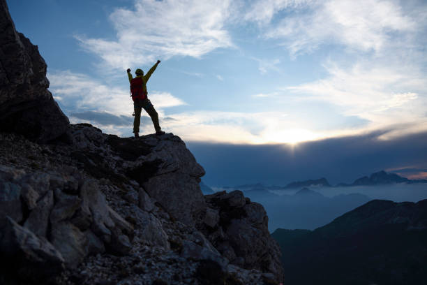 Mountain climber on the top with hands in the air enjoying the view. Back ligth by setting sun. Silhouette on the top of the mountain.