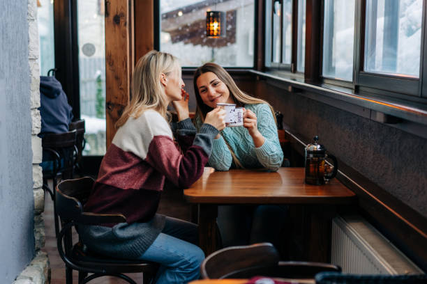 two young attractive women are chatting and drinking coffee while sitting in a cozy bar in winter. - apres ski winter friendship ski imagens e fotografias de stock