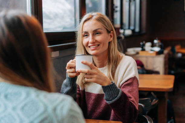 portret atrakcyjnej blondynki rozmawiającej z przyjaciółką siedzącej w przytulnej ciepłej kawiarni. - apres ski friendship skiing enjoyment zdjęcia i obrazy z banku zdjęć